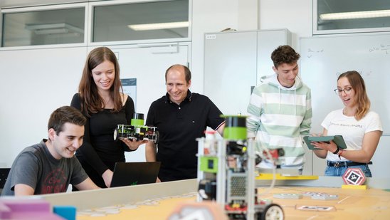 Vier Studierende begutachten mit ihrem Professor ihre Roboter-Modelle