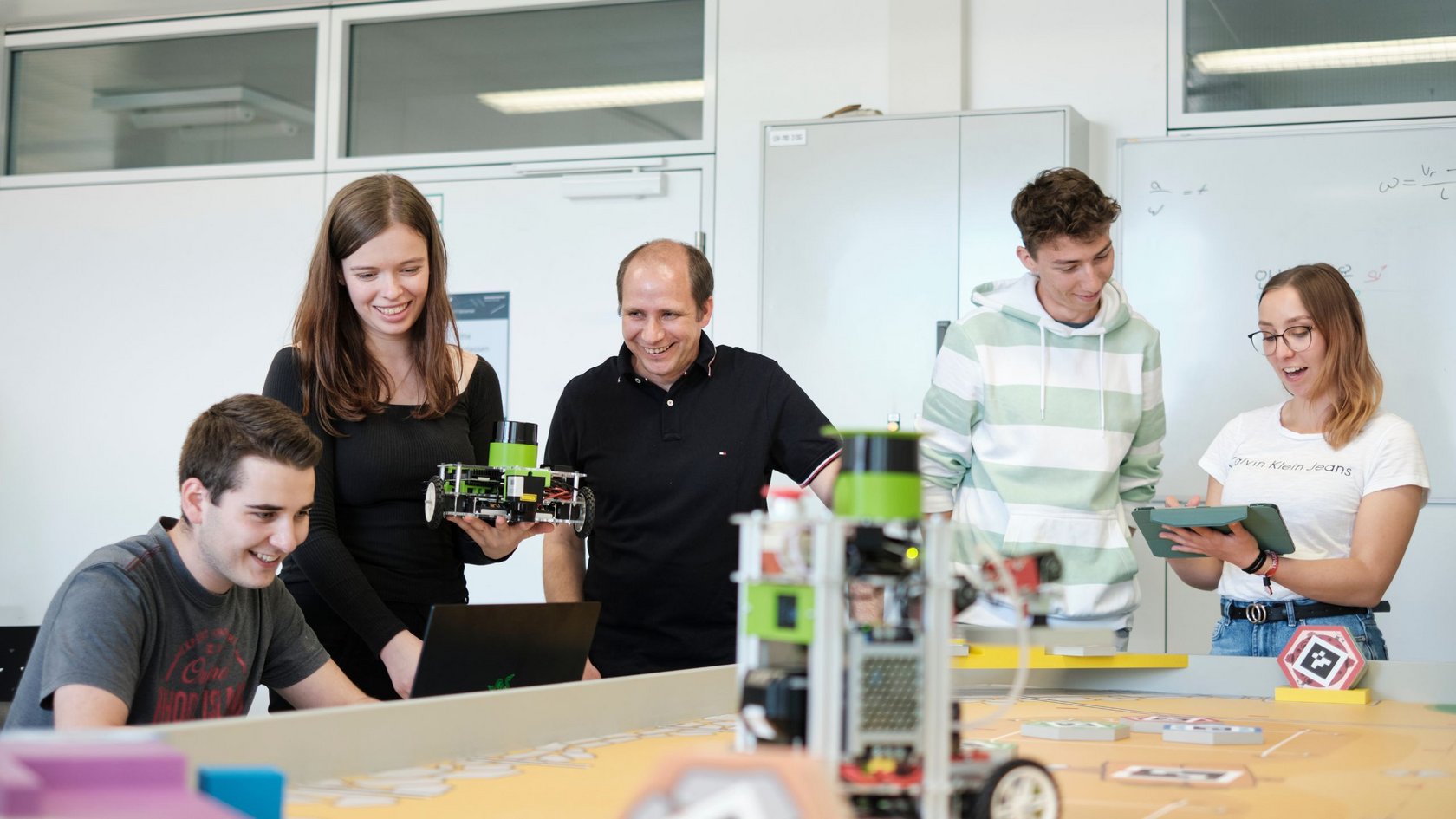 Vier Studierende begutachten mit ihrem Professor ihre Roboter-Modelle