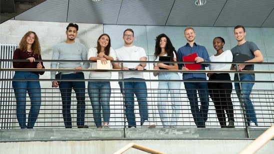 Mehrere Studierende stehen an einem Geländer und schauen lachend nach unten.