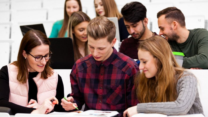 Studierende sitzen in einem Hörsaal und arbeiten gemeinsam an Notizen und Laptops