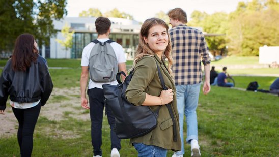 Eine Studentin läuft mit weiteren Studis auf ein Hochschulgebäude zu.