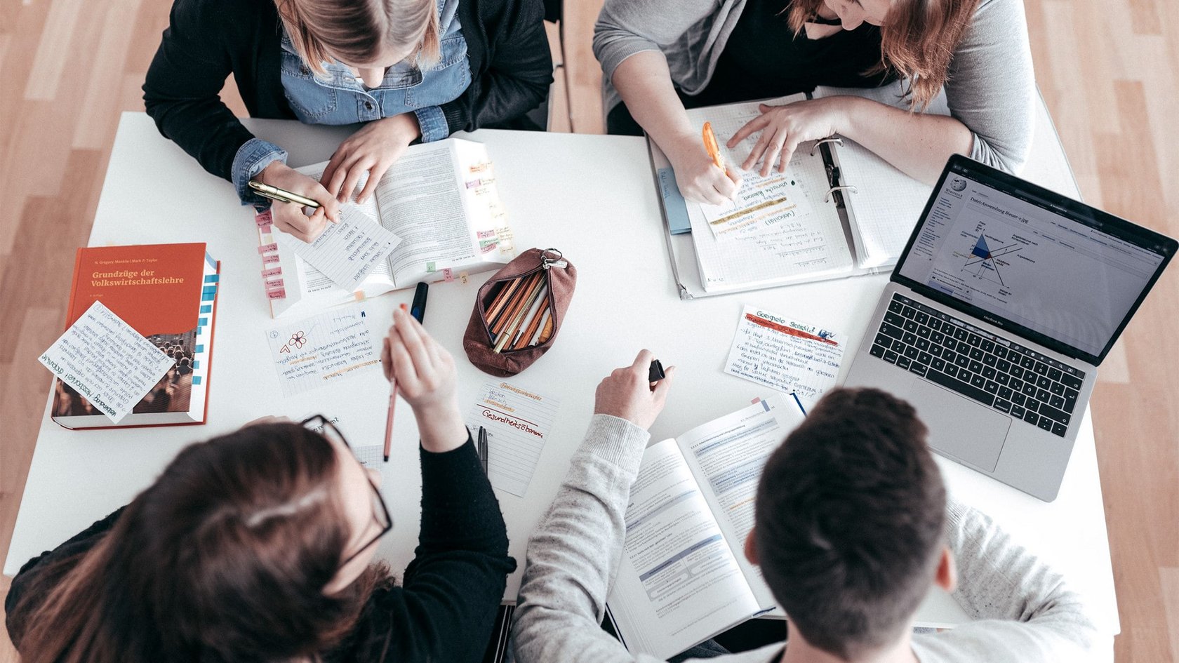 Studierende sitzen an einem Tisch und lernen gemeinsam mit Büchern, Notizzetteln und einem Laptop