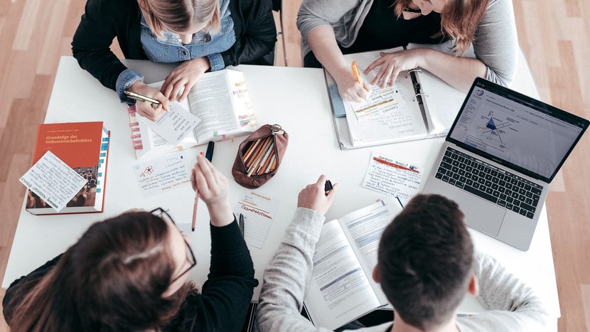 Studierende sitzen an einem Tisch und lernen gemeinsam mit Büchern, Notizzetteln und einem Laptop